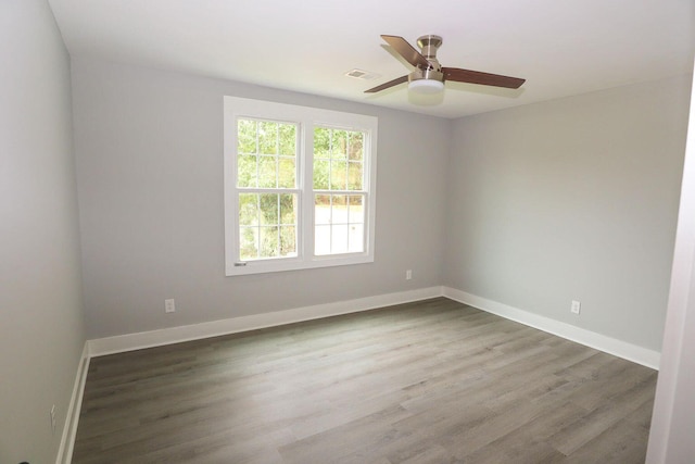 empty room featuring visible vents, wood finished floors, a ceiling fan, and baseboards