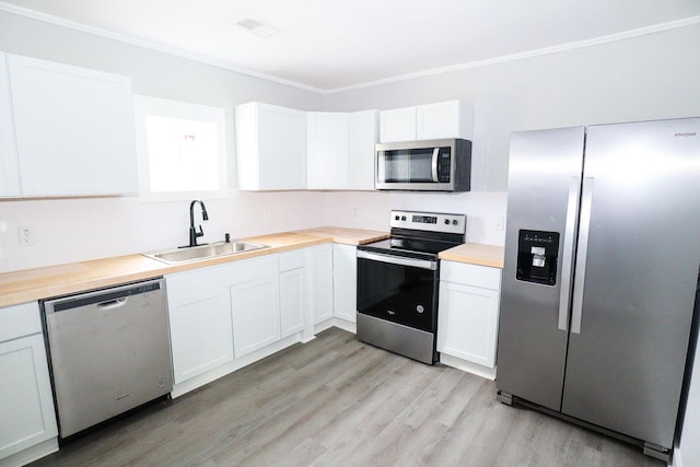 kitchen featuring white cabinets, appliances with stainless steel finishes, ornamental molding, light wood-style floors, and a sink