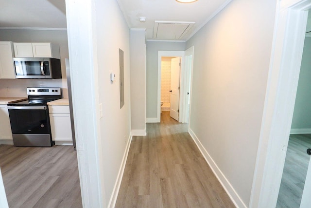 corridor with light wood finished floors, ornamental molding, attic access, and baseboards