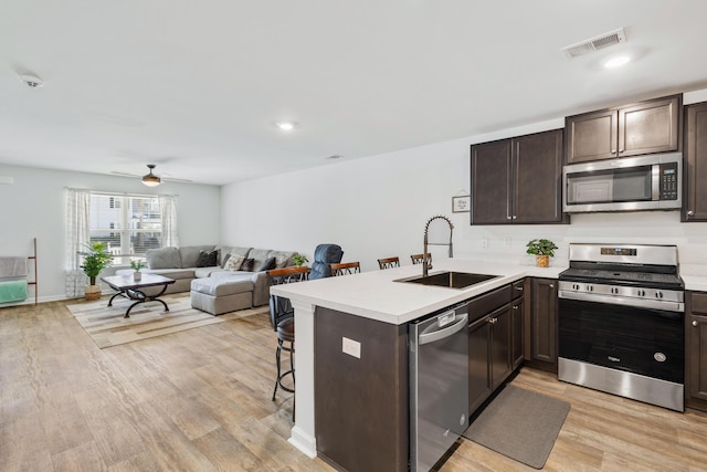 kitchen featuring light countertops, appliances with stainless steel finishes, open floor plan, a sink, and a peninsula