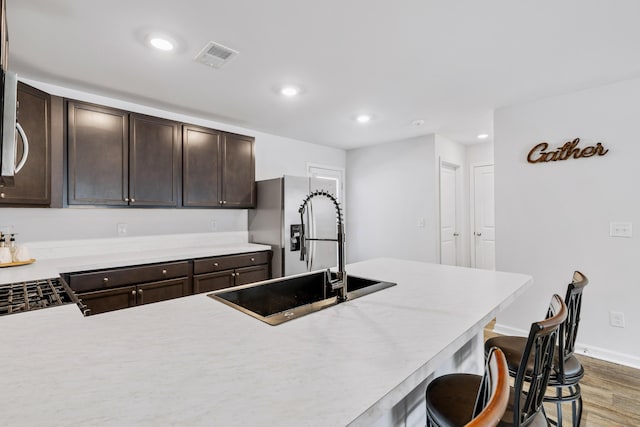 kitchen featuring visible vents, stainless steel fridge with ice dispenser, dark wood-style floors, a breakfast bar, and light countertops