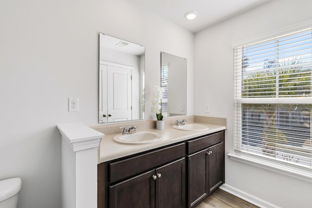 bathroom with baseboards, a sink, toilet, and double vanity