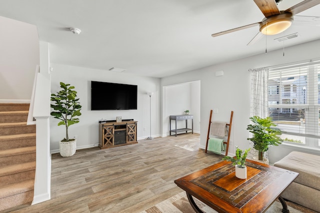 living area with light wood finished floors, visible vents, stairway, a ceiling fan, and baseboards