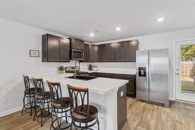 kitchen with a peninsula, appliances with stainless steel finishes, light countertops, and a kitchen breakfast bar