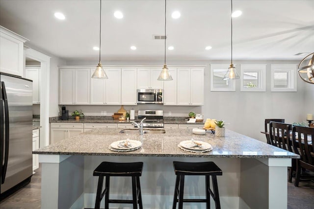 kitchen with decorative light fixtures, appliances with stainless steel finishes, and a kitchen island with sink