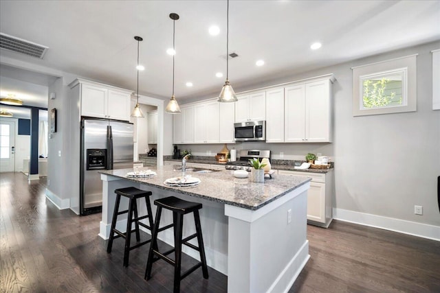 kitchen with white cabinets, pendant lighting, appliances with stainless steel finishes, and an island with sink