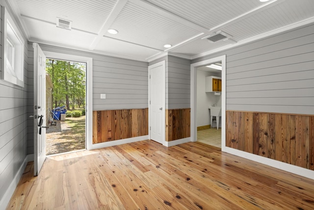 empty room with wood walls, wood-type flooring, visible vents, and baseboards