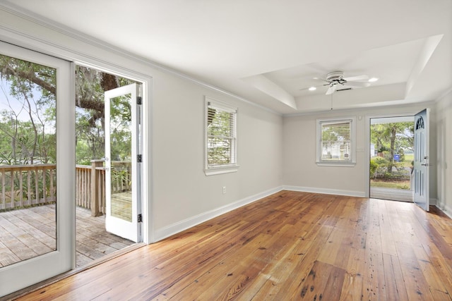 doorway to outside featuring light wood-style floors, a raised ceiling, ceiling fan, and baseboards