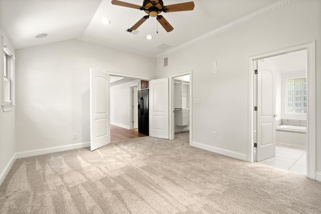 unfurnished bedroom with baseboards, a spacious closet, vaulted ceiling, black refrigerator with ice dispenser, and carpet flooring