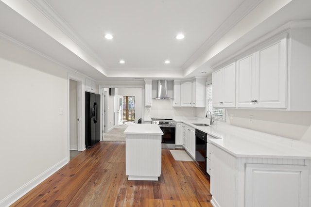 kitchen with a sink, a kitchen island, black appliances, wall chimney exhaust hood, and a raised ceiling