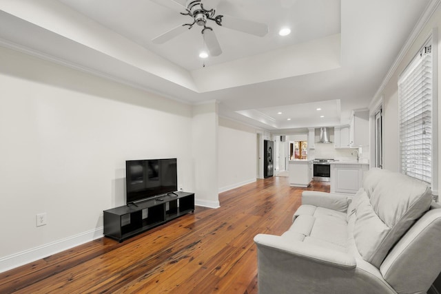 living room with ornamental molding, a tray ceiling, wood-type flooring, and baseboards