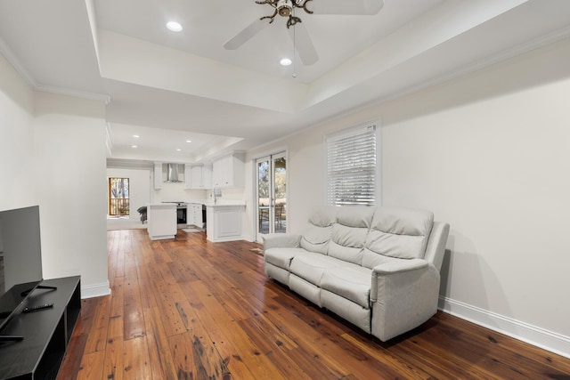 living area with recessed lighting, a raised ceiling, hardwood / wood-style floors, ornamental molding, and baseboards