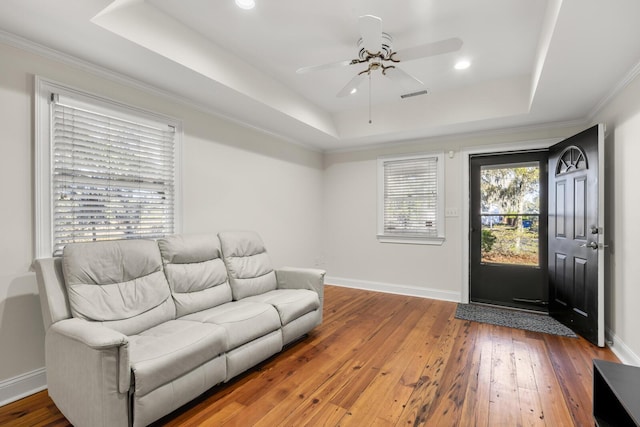 living room featuring wood-type flooring, visible vents, a raised ceiling, and baseboards