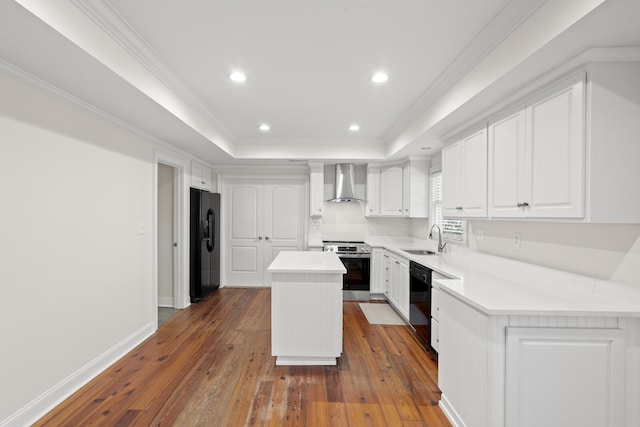 kitchen with a sink, wall chimney range hood, a center island, black appliances, and a tray ceiling