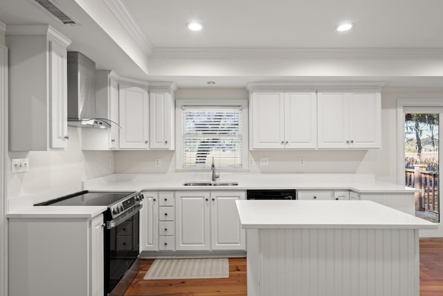 kitchen with dark wood finished floors, wall chimney range hood, crown molding, stainless steel range with electric stovetop, and a sink