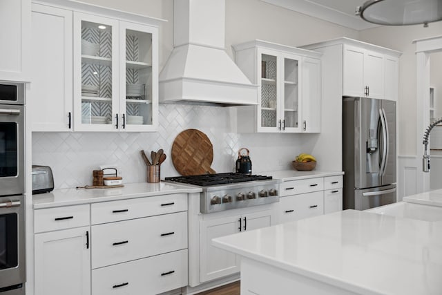kitchen with stainless steel appliances, light countertops, custom range hood, white cabinetry, and tasteful backsplash