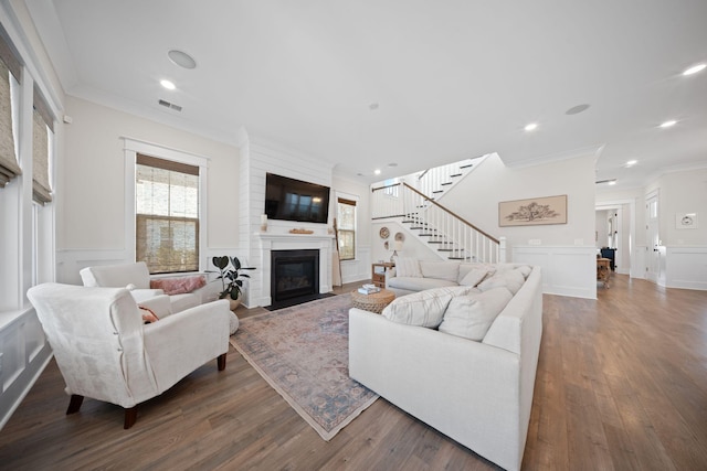 living room with visible vents, ornamental molding, wood finished floors, a large fireplace, and stairs