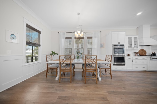 dining area with crown molding, a chandelier, a wainscoted wall, wood finished floors, and a decorative wall
