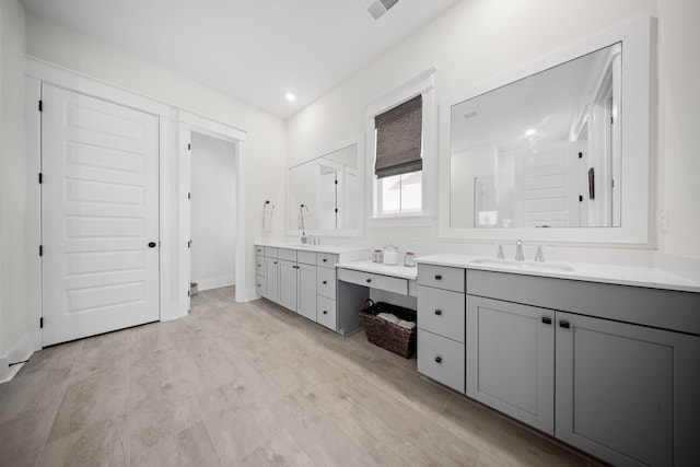 full bath with a sink, baseboards, two vanities, and wood finished floors