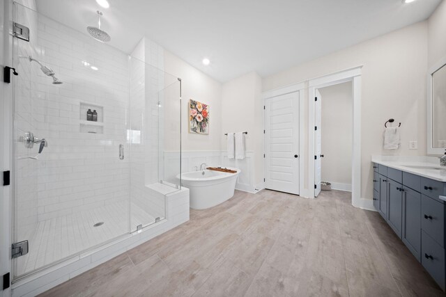bathroom with a freestanding tub, a stall shower, wood finished floors, recessed lighting, and vanity