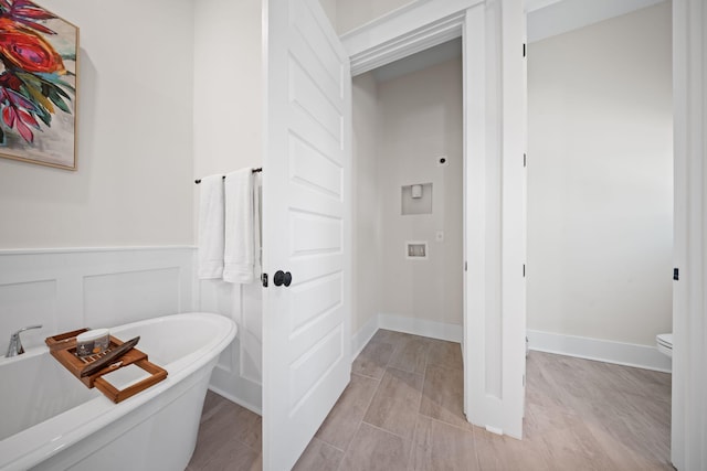 bathroom with wood finish floors, a freestanding bath, wainscoting, a decorative wall, and toilet