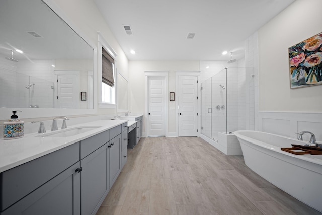 full bath featuring vanity, wood finished floors, a wainscoted wall, visible vents, and a stall shower