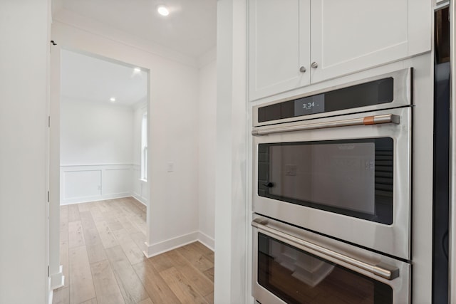 kitchen featuring light hardwood / wood-style floors, white cabinetry, crown molding, and double oven