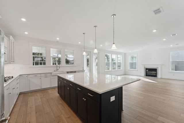 kitchen with sink, a kitchen island, light hardwood / wood-style flooring, decorative light fixtures, and white cabinets