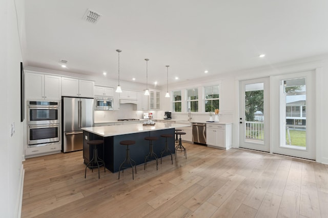 kitchen with a breakfast bar, a center island, white cabinets, light wood-type flooring, and appliances with stainless steel finishes