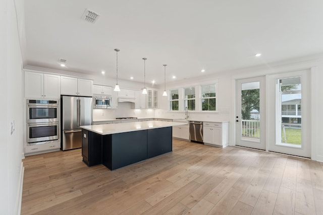 kitchen with white cabinetry, a center island, light hardwood / wood-style flooring, pendant lighting, and appliances with stainless steel finishes