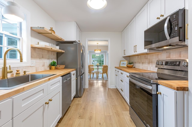 kitchen with light wood-type flooring, white cabinets, a sink, stainless steel appliances, and wood counters