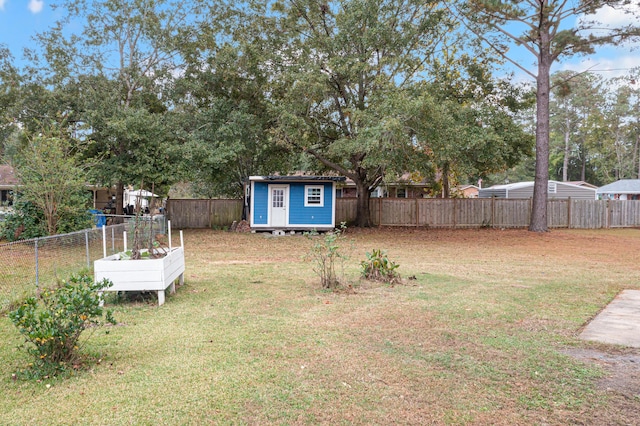 view of yard with a garden, a fenced backyard, an outdoor structure, and a storage unit
