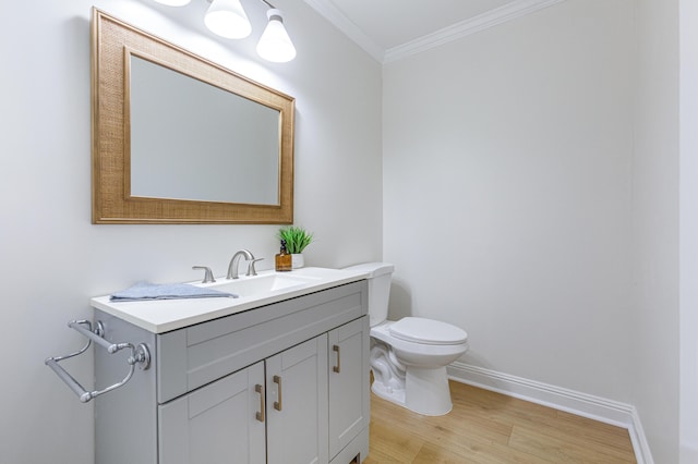 half bathroom featuring vanity, ornamental molding, toilet, wood finished floors, and baseboards