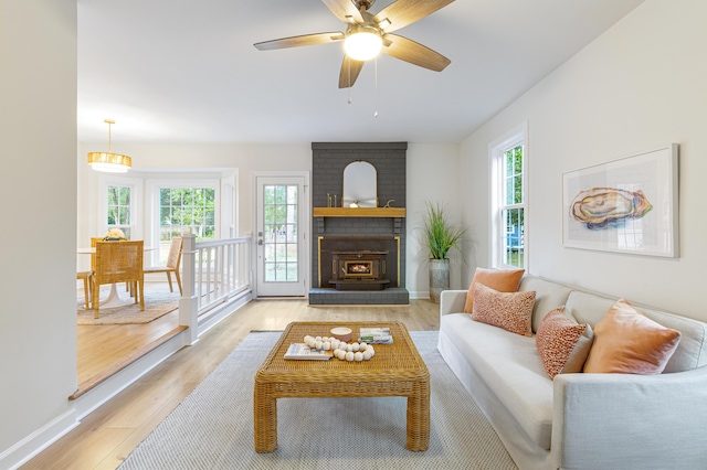 living area with light wood-style floors, baseboards, a ceiling fan, and a brick fireplace