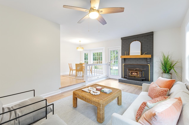 living room with baseboards, a brick fireplace, light wood-type flooring, and a ceiling fan