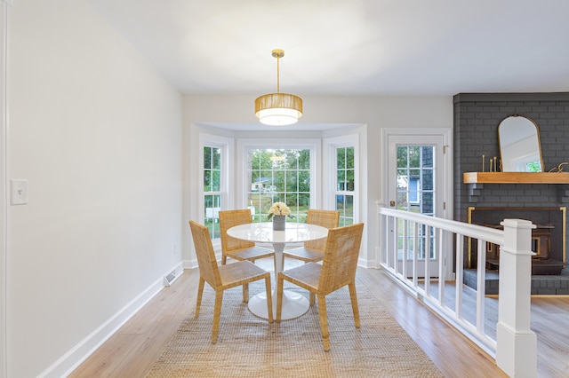 dining area with wood finished floors, baseboards, visible vents, and a brick fireplace