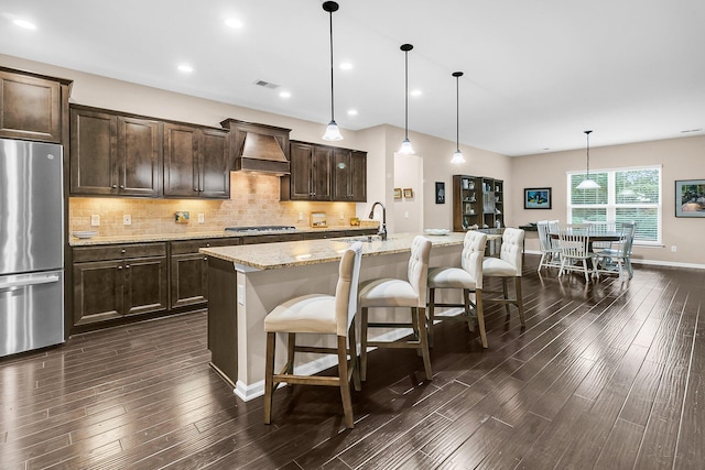 kitchen featuring pendant lighting, dark brown cabinets, a kitchen island with sink, appliances with stainless steel finishes, and a kitchen bar