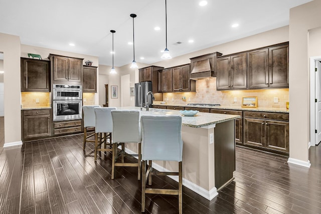 kitchen featuring hanging light fixtures, a breakfast bar area, dark hardwood / wood-style flooring, dark brown cabinetry, and a kitchen island with sink