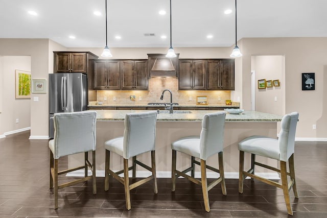 kitchen with light stone counters, a kitchen island with sink, decorative light fixtures, and dark wood-type flooring