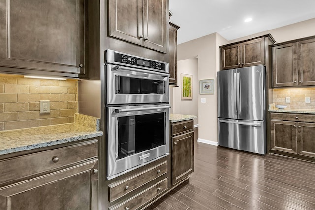 kitchen with dark brown cabinets, stainless steel appliances, light stone counters, and dark hardwood / wood-style flooring