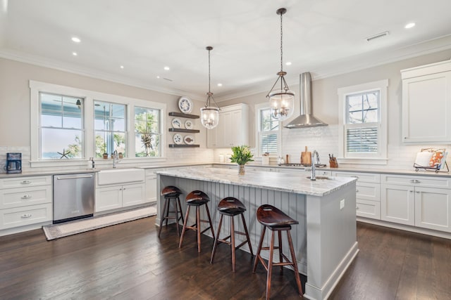 kitchen with visible vents, a center island with sink, a sink, stainless steel appliances, and wall chimney exhaust hood