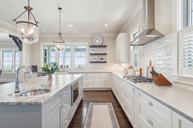 kitchen featuring range hood, a sink, stainless steel gas stovetop, white cabinetry, and crown molding