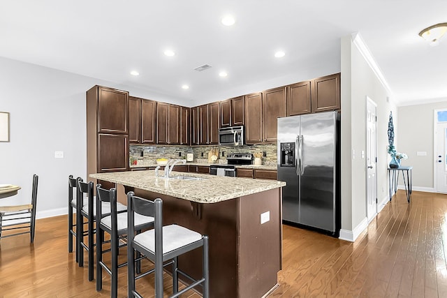 kitchen featuring dark hardwood / wood-style floors, an island with sink, sink, a breakfast bar, and appliances with stainless steel finishes