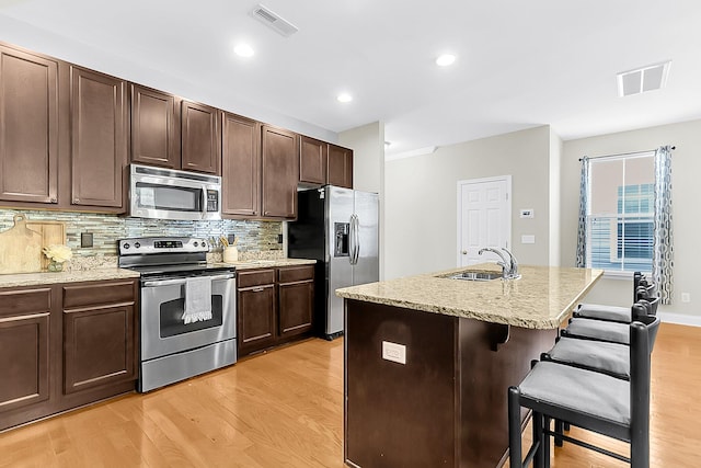 kitchen with tasteful backsplash, a breakfast bar, a kitchen island with sink, light hardwood / wood-style flooring, and stainless steel appliances