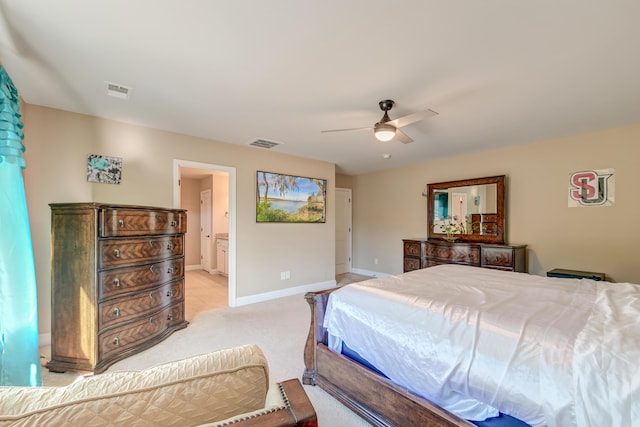 bedroom with ceiling fan, light colored carpet, and ensuite bath