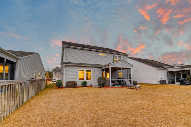 back house at dusk featuring a lawn and cooling unit