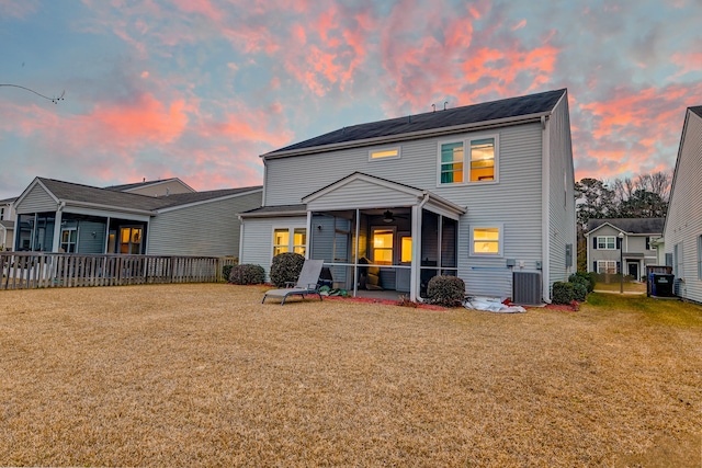 back house at dusk featuring a sunroom, ceiling fan, cooling unit, and a lawn