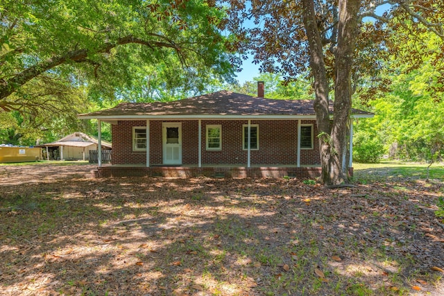 ranch-style home featuring covered porch, a chimney, and brick siding