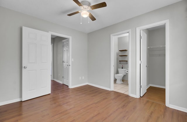 unfurnished bedroom with connected bathroom, a walk in closet, a closet, ceiling fan, and hardwood / wood-style floors