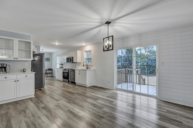 kitchen featuring sink, hanging light fixtures, light wood-type flooring, stainless steel appliances, and white cabinets